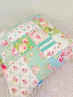 a patchwork pillow is sitting on a lace tablecloth with pink and green flowers