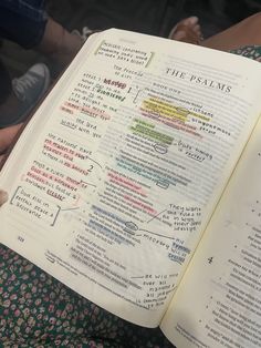 an open bible with words written on it and people sitting in the background holding up their hands