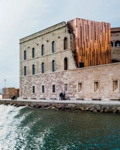 two people standing on the side of a body of water next to a large building