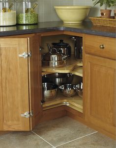 an open cabinet in a kitchen with pots and pans on the counter top,