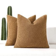 two brown pillows sitting on top of a white couch next to a green cactus plant