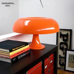 an orange lamp sitting on top of a table next to some books and a framed photograph