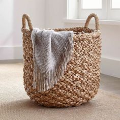 a woven basket with a blanket on the floor in front of a white wall and window