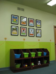 an empty room with green walls and pictures on the wall above shelves filled with toys