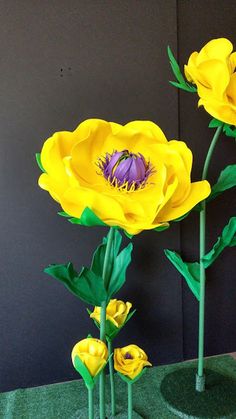 three yellow flowers sitting on top of a green table next to a black wall and grass