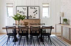 a dining room table with black chairs and pictures on the wall above it, along with a blue striped rug