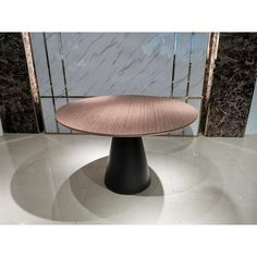 a round wooden table sitting on top of a white floor in front of a marble wall