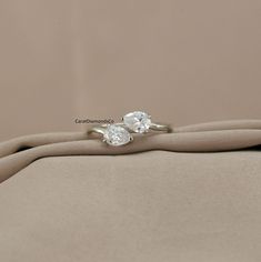 two engagement rings sitting on top of a cloth covered cushioned surface, with one diamond set in the middle