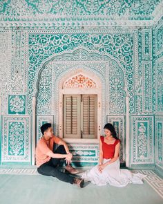 a man and woman sitting on the ground in front of a building with intricately painted walls