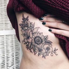 a woman's stomach with sunflowers and leaves tattoo on her side ribcage