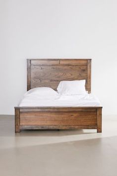 a wooden bed frame with white sheets and pillows