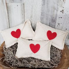 three pillows with red hearts on them sitting in a bowl filled with grass and twigs