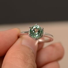 a close up of a person's hand holding a ring with a green stone