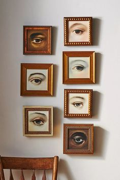 several framed pictures hang on the wall above a wooden chair in front of an eyeball