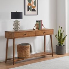 a wooden table with two drawers and a lamp on it next to a potted plant