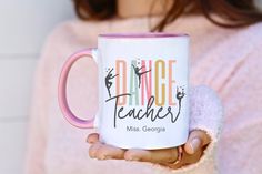 a woman holding a pink and white coffee mug with the words dance teacher on it