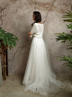 a woman standing in front of a wall wearing a white wedding dress with long sleeves