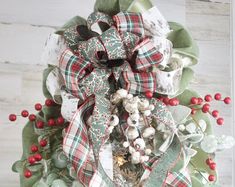 a christmas wreath with red berries and green ribbon hanging from the front of a door