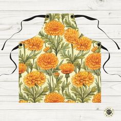 an orange flowered apron with black straps on a white wooden background, featuring yellow flowers and green leaves