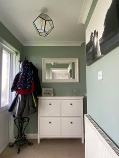 a white dresser sitting under a mirror next to a window in a room with green walls