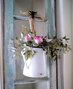 a white watering can with pink roses and greenery in it hanging from an old door