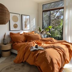 a bed with orange sheets and pillows in a bedroom next to a large window that has pictures on the wall