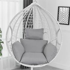 a white hanging chair with grey cushions in a living room area next to a potted plant