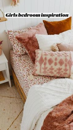 a bed covered in lots of pillows next to a white table with flowers on it