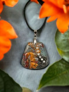 a close up of a pendant on a necklace with flowers in the background and an orange flower