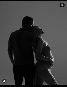 a man and woman standing next to each other in black and white photo with their arms around each other