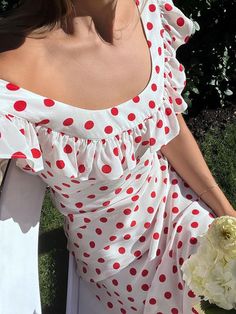 a woman in a polka dot dress sitting on a chair holding a white flower and looking off to the side