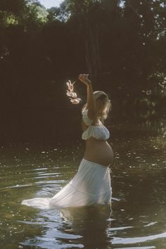 a pregnant woman standing in the water with her hands up