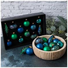 a wooden bowl filled with blue and green ornaments next to a black box on a table