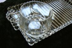 a clear glass sitting on top of a black table next to a metal tray with beads