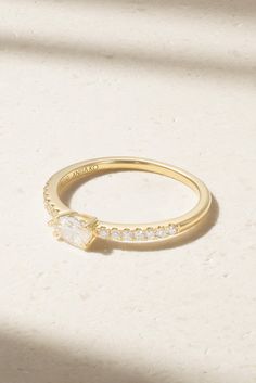 a yellow gold ring with white stones on it and a shadow from the window behind it