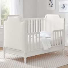 a white baby crib in a room with pink carpet and pictures on the wall