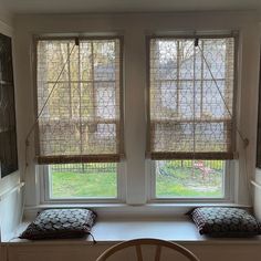 two windows with matching blinds in the same room, one has a cushion on it