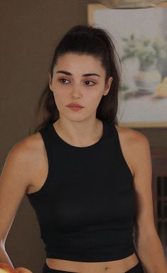 a young woman holding an apple in her right hand and looking at the camera while wearing a black crop top