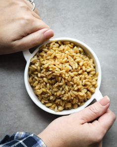 a person holding a bowl full of brown rice on top of a gray countertop