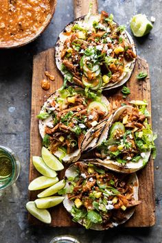 three tacos with shredded meat, avocado and cilantro on a cutting board