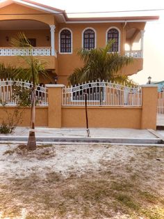 an orange house with white fence and palm trees in the front yard on a sunny day