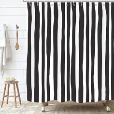 a black and white shower curtain hanging on a wall next to a wooden stool in a bathroom