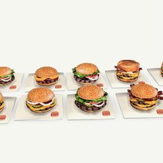 several hamburgers are arranged in rows on white plates