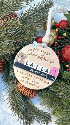 a personalized ornament hanging from a christmas tree with pine cones and ornaments