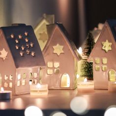 three small houses with lit candles in front of them on a table next to a christmas tree