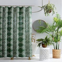 a green shower curtain next to two potted plants and a mirror on the wall