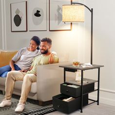 a man and woman sitting on a couch in a living room with modern art behind them