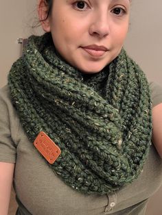 a woman wearing a green knitted cowl with a brown leather tag on it