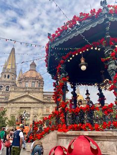 people are gathered around an elaborate gazebo decorated with red flowers and garlanded with lights