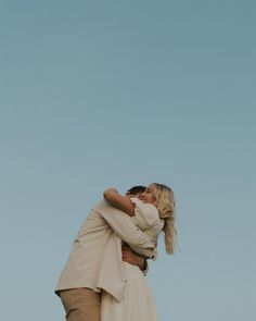 a man and woman embracing each other in front of a blue sky with no clouds